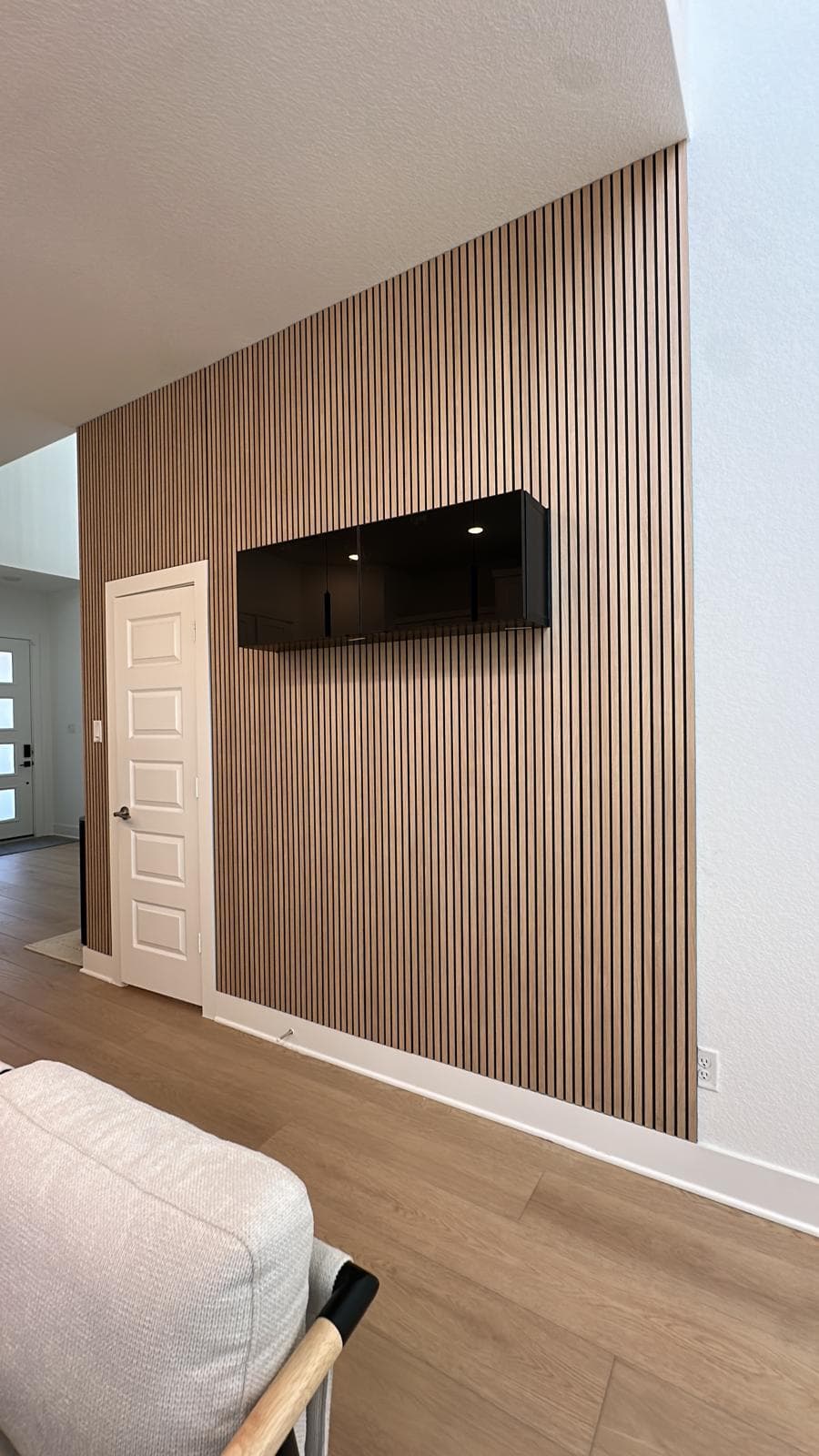 Black floating cabinet mounted on a vertical wood slat accent wall in a modern interior.