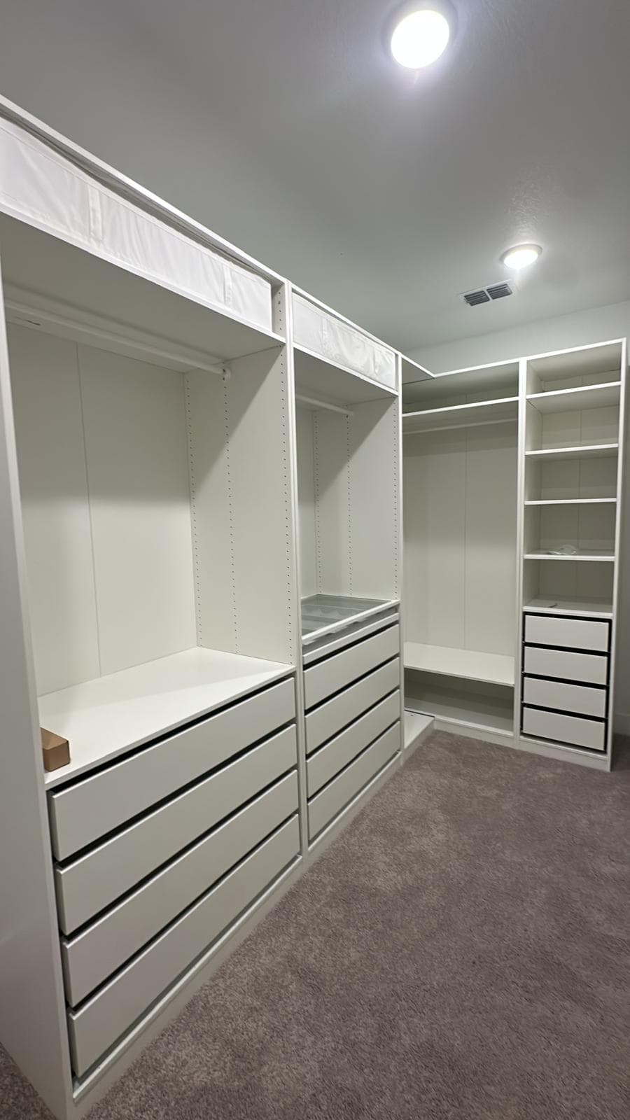 Modern white custom walk-in closet featuring drawers, shelves, and hanging rods on grey carpet.